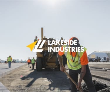 Construction worker shoveling material with machinery and crew in background