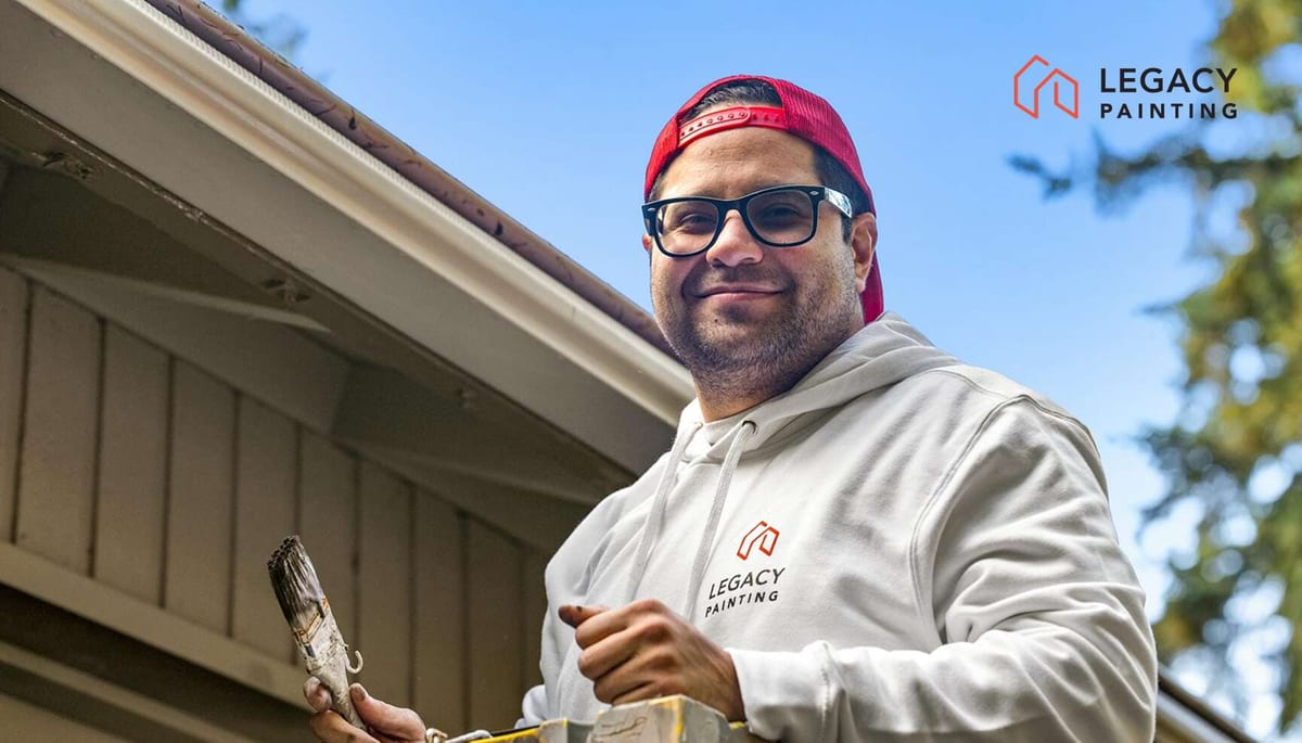 Legacy Painting owner in white hoodie holding paintbrush and ladder outside a house